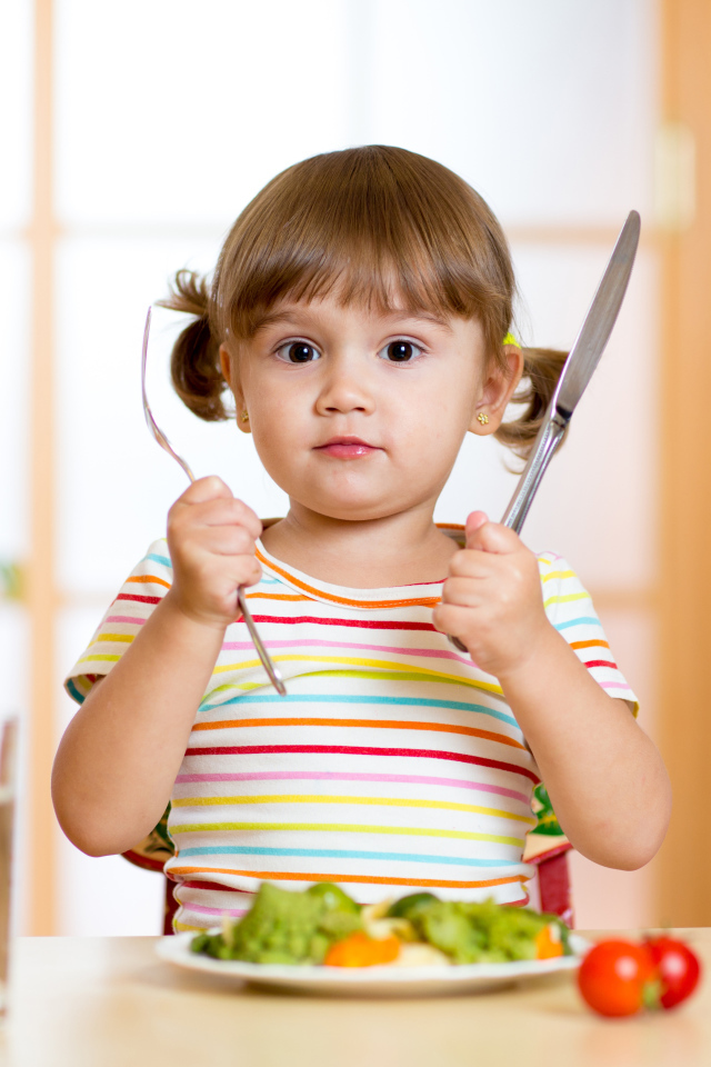 A little girl with cutlery and a plate