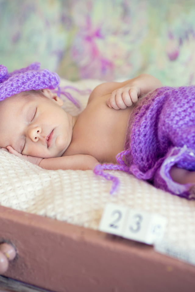 A little sleeping baby in a knitted purple suit