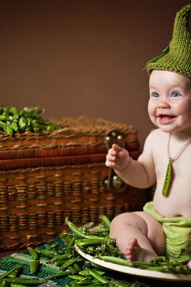 Забавный улыбающийся малыш сидит на стручках зеленого гороха