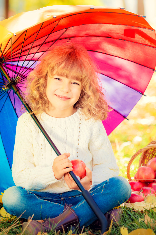 Улыбающаяся девочка с корзиной яблок сидит под разноцветным зонтом