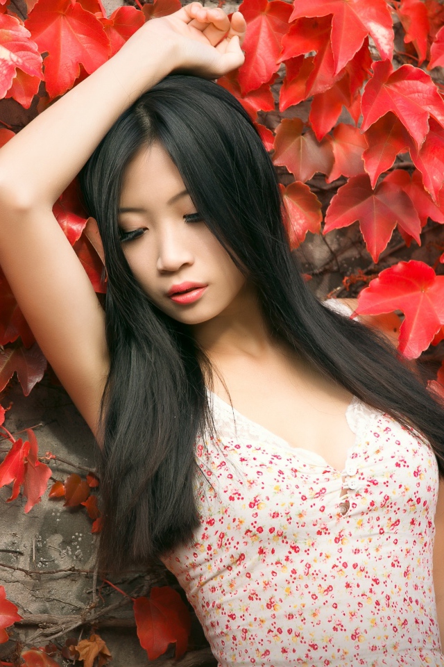 Молодая девушка азиатка стоит у стены с красными листьями