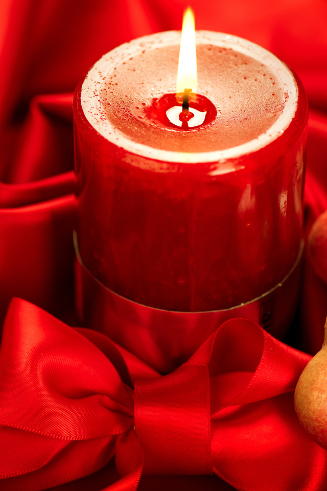 Зажженная свеча с двумя сердечками на красном фоне с бантом