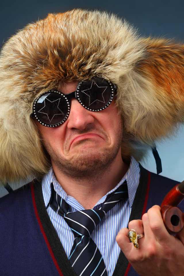 A man in a fur hat wearing fashionable glasses with a pipe in his hand
