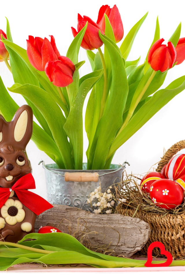 Букет красных тюльпанов на столе с шоколадным кроликом и крашеными яйцами на Пасху