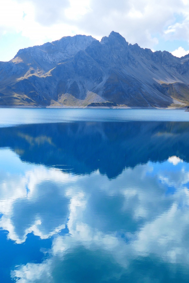 Красивые белые облака отражаются в воде озера на фоне гор 