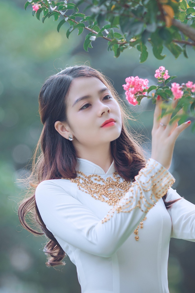 Красивая азиатка в белом платье у ветки с розовыми цветами