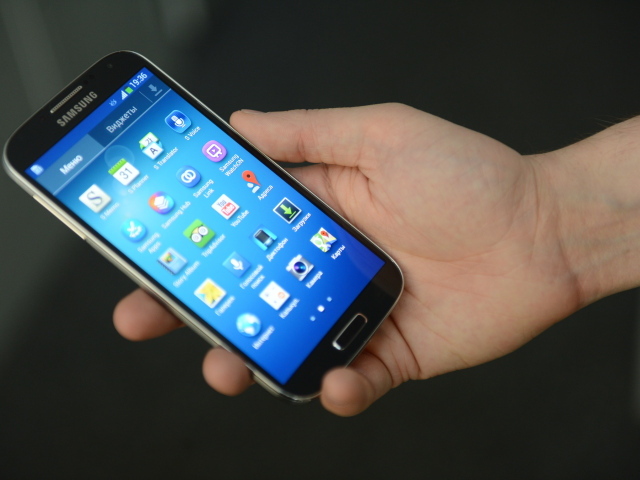 Samsung Galaxy S4 в руке на сером фоне