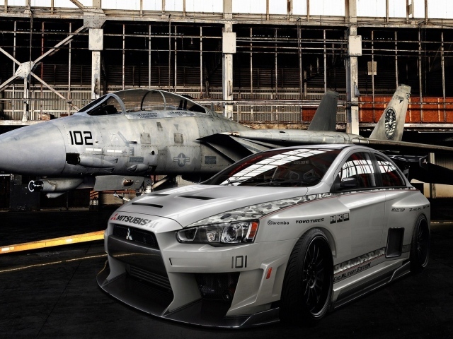 Серый гоночный Mitsubishi в ангаре с самолетом
