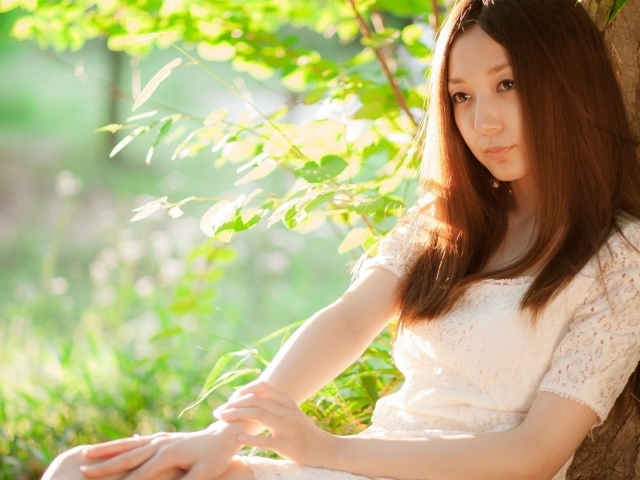 Азиатская девушка прислонилась спиной к дереву