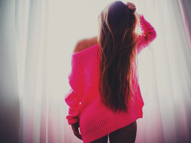Брюнетка в розовой кофте стоит у окна