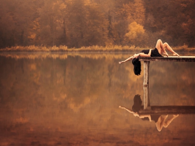 Брюнетка лежит на пирсе на озере