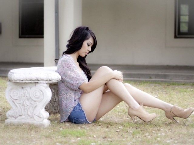 Брюнетка сидит на земле у каменной скамьи