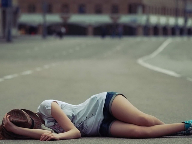 Девушка в шляпе лежит на дороге