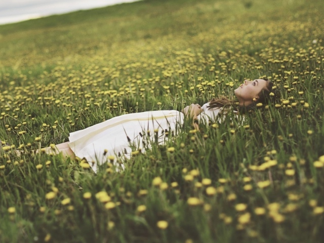 Девушка лежит в поле среди одуванчиков