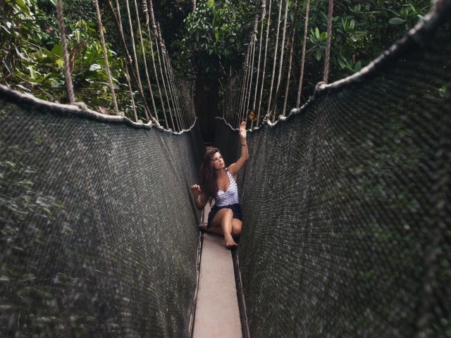 Девушка сидит на подвесном мосту