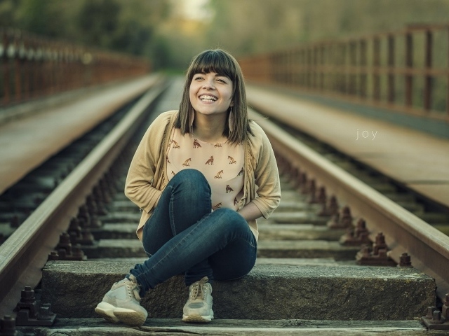 Девушка улыбается сидя на рельсах