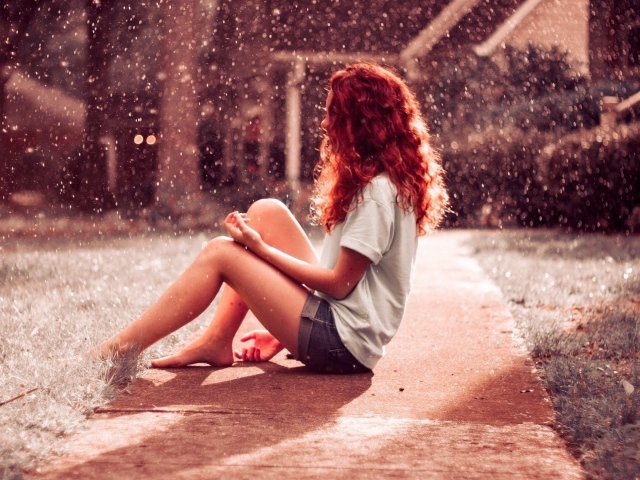 Рыжая девушка сидит на земле во время дождя