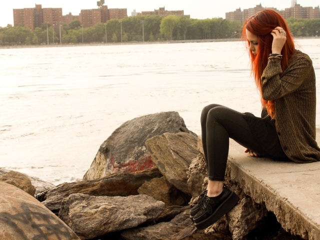 Рыжая девушка сидит на плитах набережной