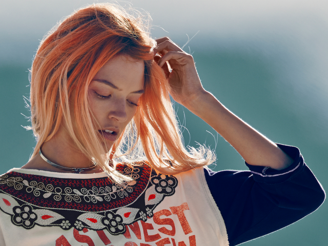 Рыжая девушка на ветру поправляет волосы