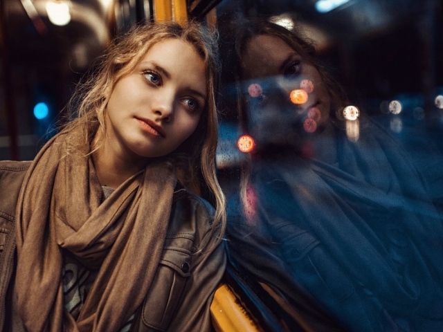 Девушка прислонилась к окну вечернего автобуса