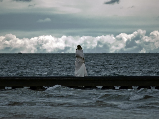 Девушка смотрит на свинцовые воды моря