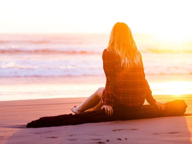 Девушка на сидит на пляже во время заката