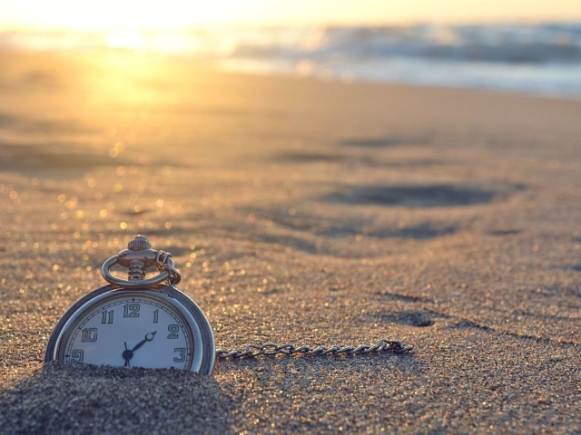 Часы на цепочке лежат в песке