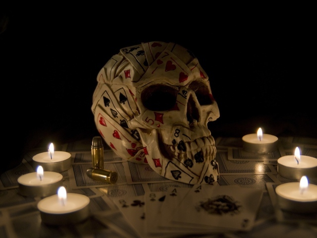 Череп из игровых карт среди свечей
