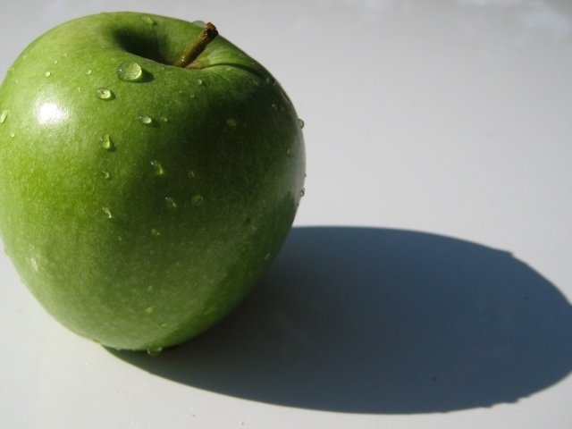 Зеленое яблоко на белой поверхности