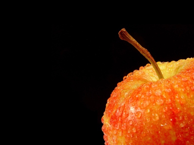 Влажное оранжевое яблоко на черном фоне