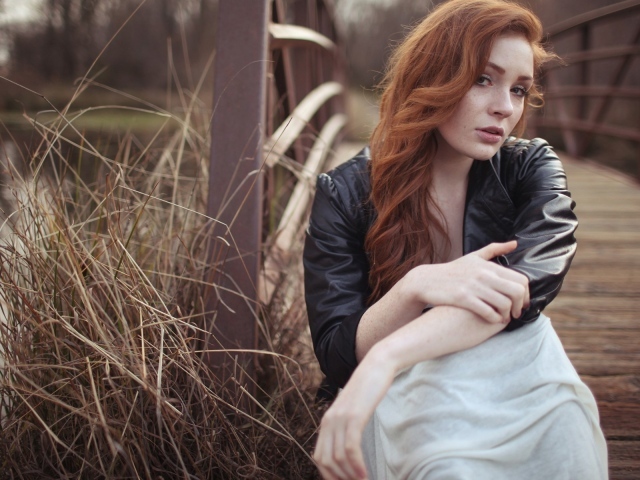 Девушка в кожаной куртке сидит у деревянного моста