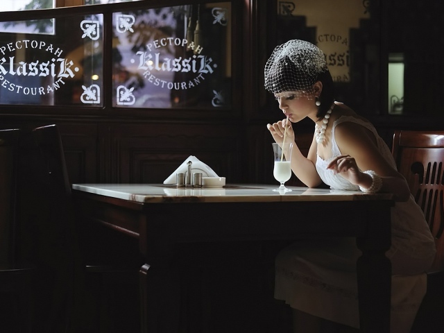 Девушка в белом платье пьет коктейль в ресторане