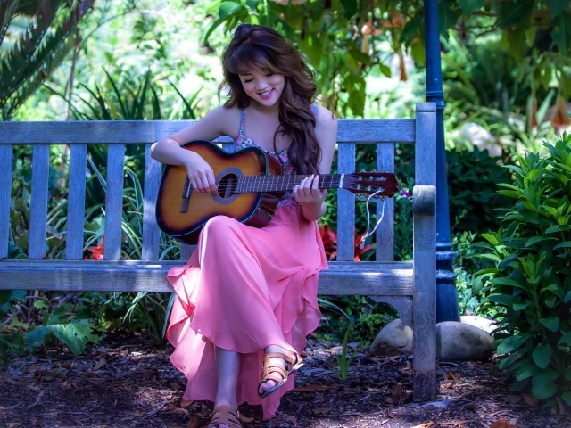 Девушка сидит на скамье в саду и играет на гитаре