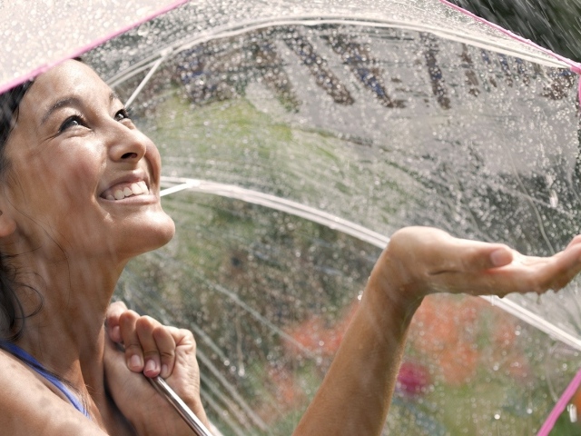 Девушка под прозрачным зонтом ловит дождь рукой