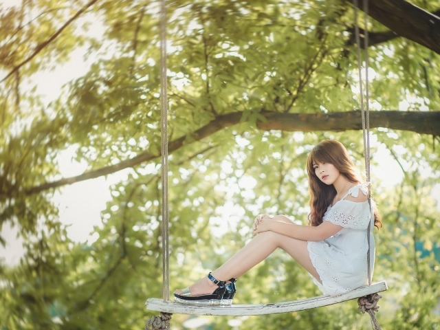 Японская девушка в белом платье сидит на качелях