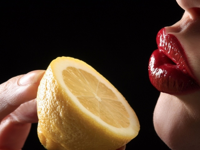 Девушка поднесла лимон к губам