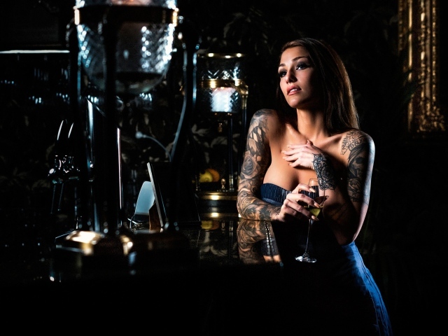 Татуированная девушка пьет вино в баре