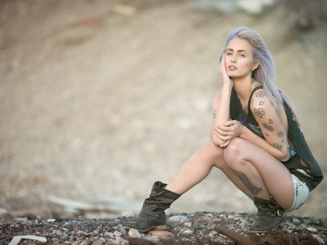 Девушка с татуировками в форме цветов сидит на корточках