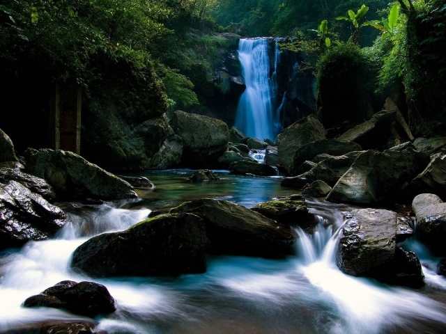 Голубой водопад позади камней на реке