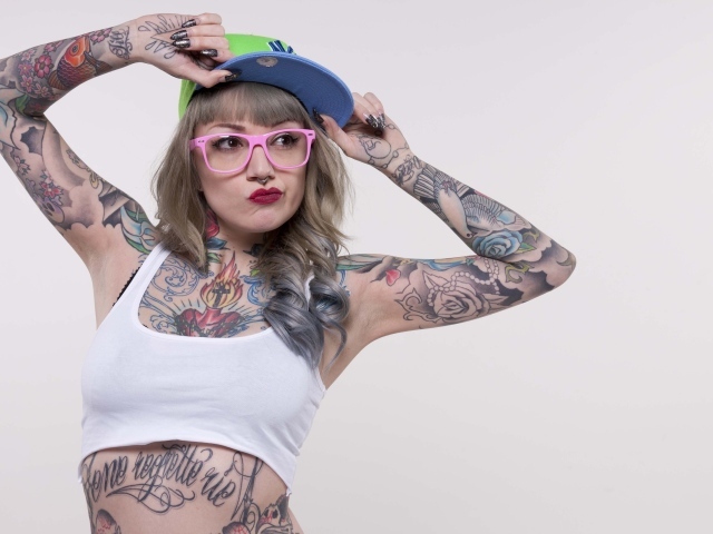 Татуированная девушка в кепке и розовых очках