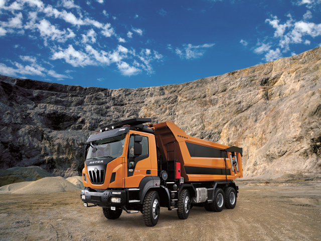 Оранжевый грузовик Astra HD9 84.50 8×4 в карьере под голубым небом