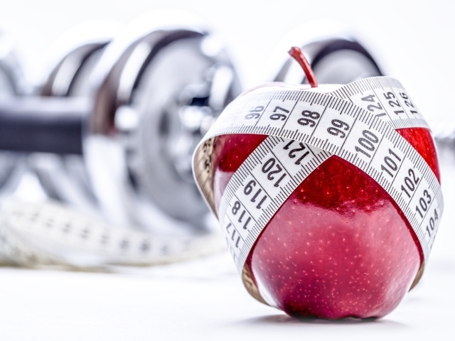 Красное яблоко перемотано мерной лентой и гантели на белом фоне