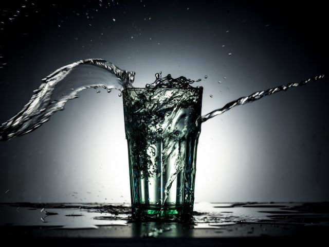 Брызги воды из стакана с водой на сером фоне