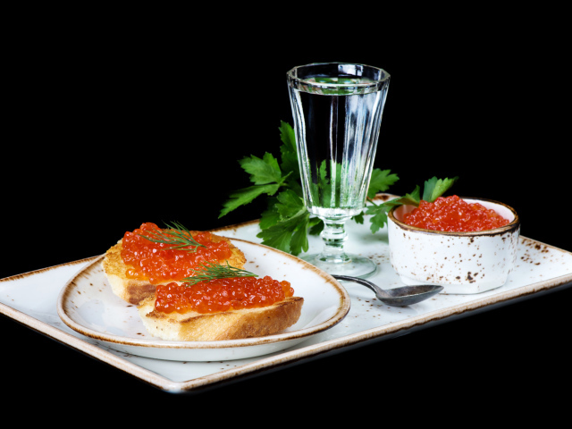 Рюмка водки, бутерброды с красной икрой и петрушка на столе