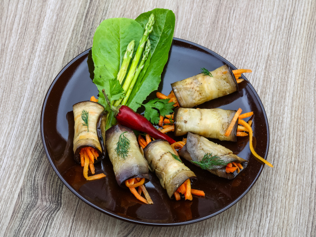 Рулетики из баклажанов с морковью на тарелке с листьями салата