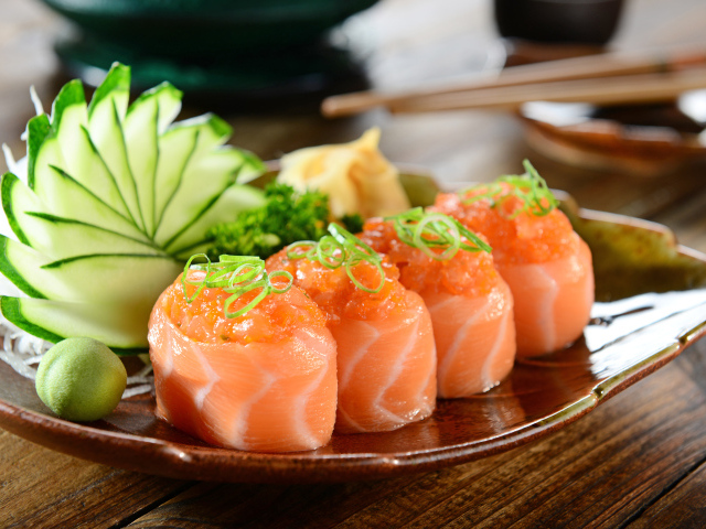 Суши из красной рыбы на тарелке со свежими огурцами и зеленью