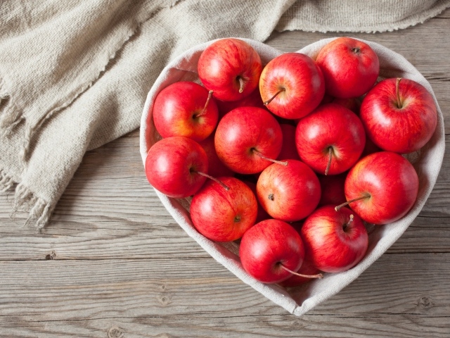 Красивые красные яблоки в тарелке в форме сердца на столе
