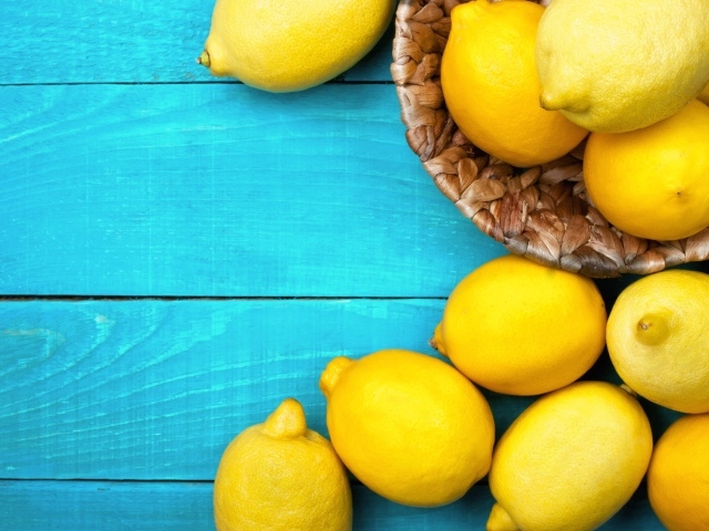Свежие желтые лимоны лежат на голубой поверхности стола