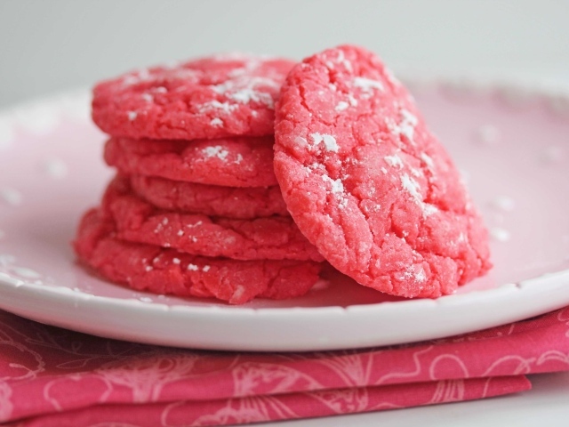 Печенье розового цвета на белой тарелке с сахарной пудрой