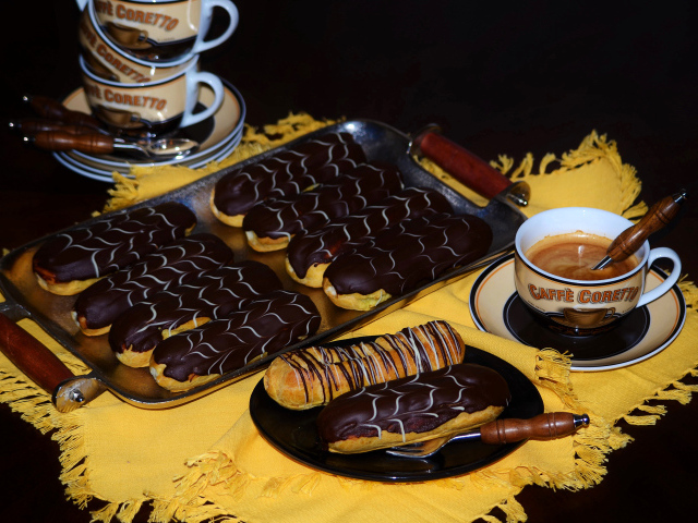 Аппетитные сладкие эклеры с шоколадом и чашками кофе на столе
